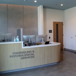 Front desk of a Counseling and Psychological Services office with computer monitors, sanitizer, and a check-in kiosk in a modern lobby.